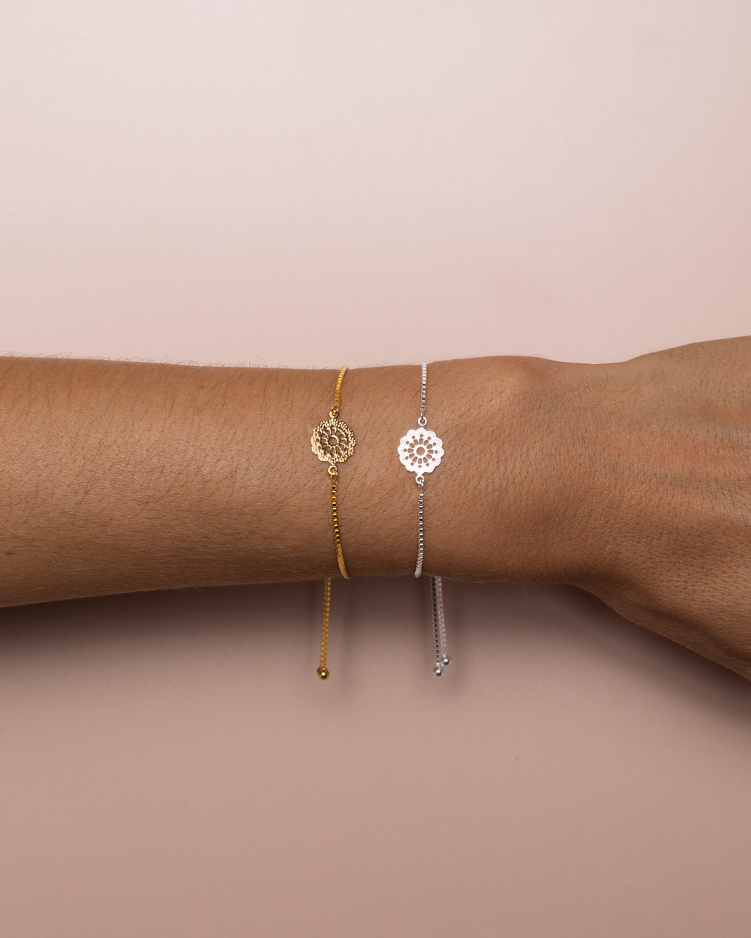 Two adjustable bracelets, one in Gold and one in Silver with a decorative clasp and small daisy charm, shown on models arm. 