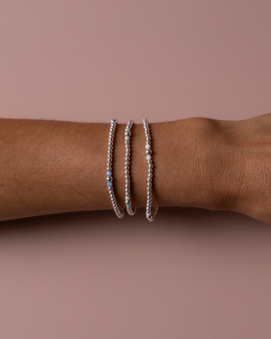 Three sterling silver, beaded bracelets on a wrist against a plain background